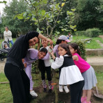 sechs Kinder und eine Betreuerin halten den frisch gepflanzten Apfelbaum am Stamm und strahlen Richtung Kamera